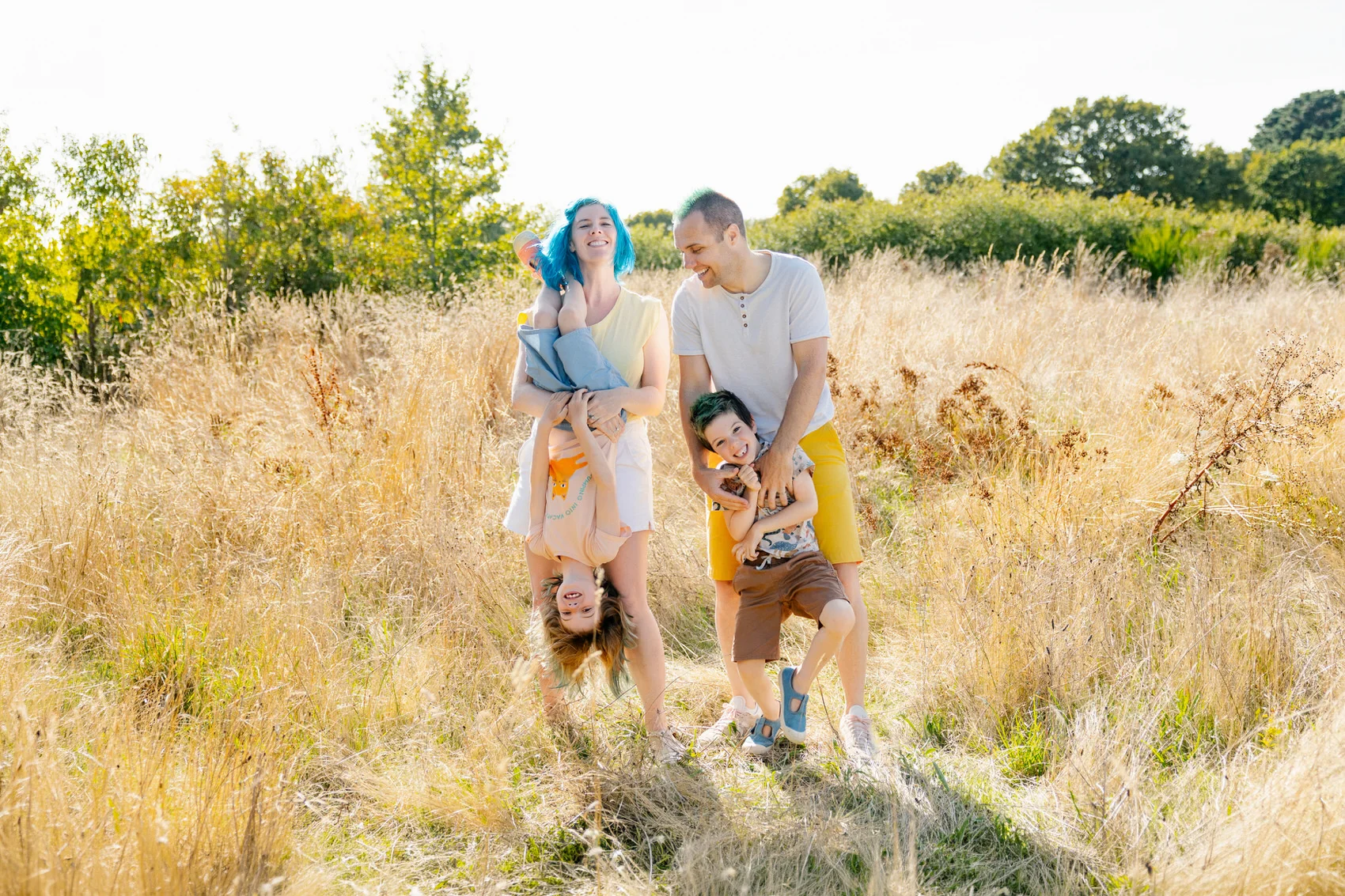 Séance photo famille dans le Morbihan, parents et enfants riant dans un champ d'herbes hautes en été