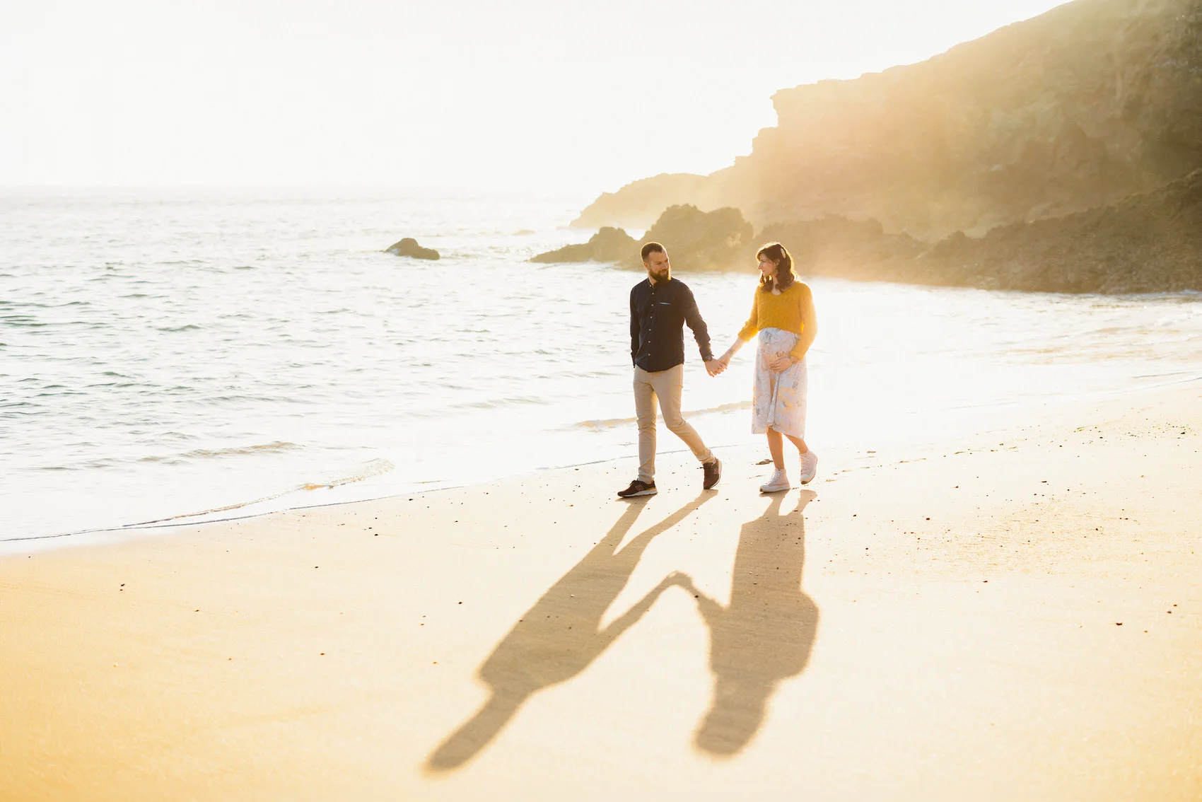 Séance grossesse sur la plage au Pouliguen, couple marchant main dans la main au soleil couchant