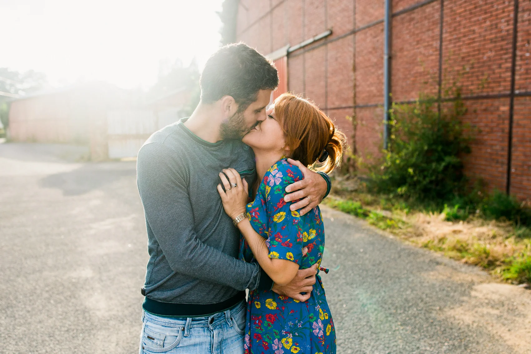Séance photo couple à Nantes, baiser en contre-jour dans une rue au décor industriel, robe fleurie bleue